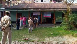 Police personnel stand guard while voters wait in a queue to cast their votes for the first phase of Manipur Assembly elections, at a polling booth, in Kangpokpi on Monday.