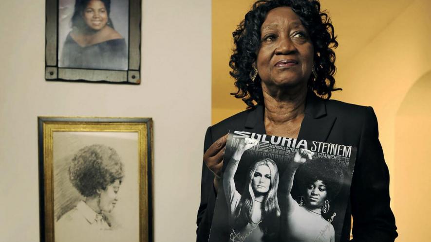 Dorothy Pitman Hughes is pictured in her home in 2013, with a poster using a 1970s image of herself and Gloria Steinem.